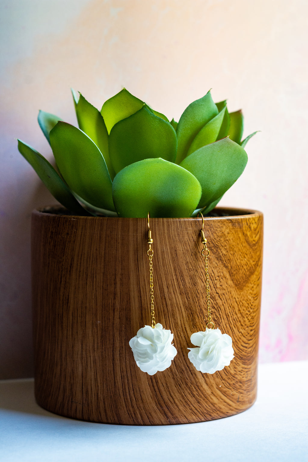 Pair of white pompom earrings hanging from a plant pot