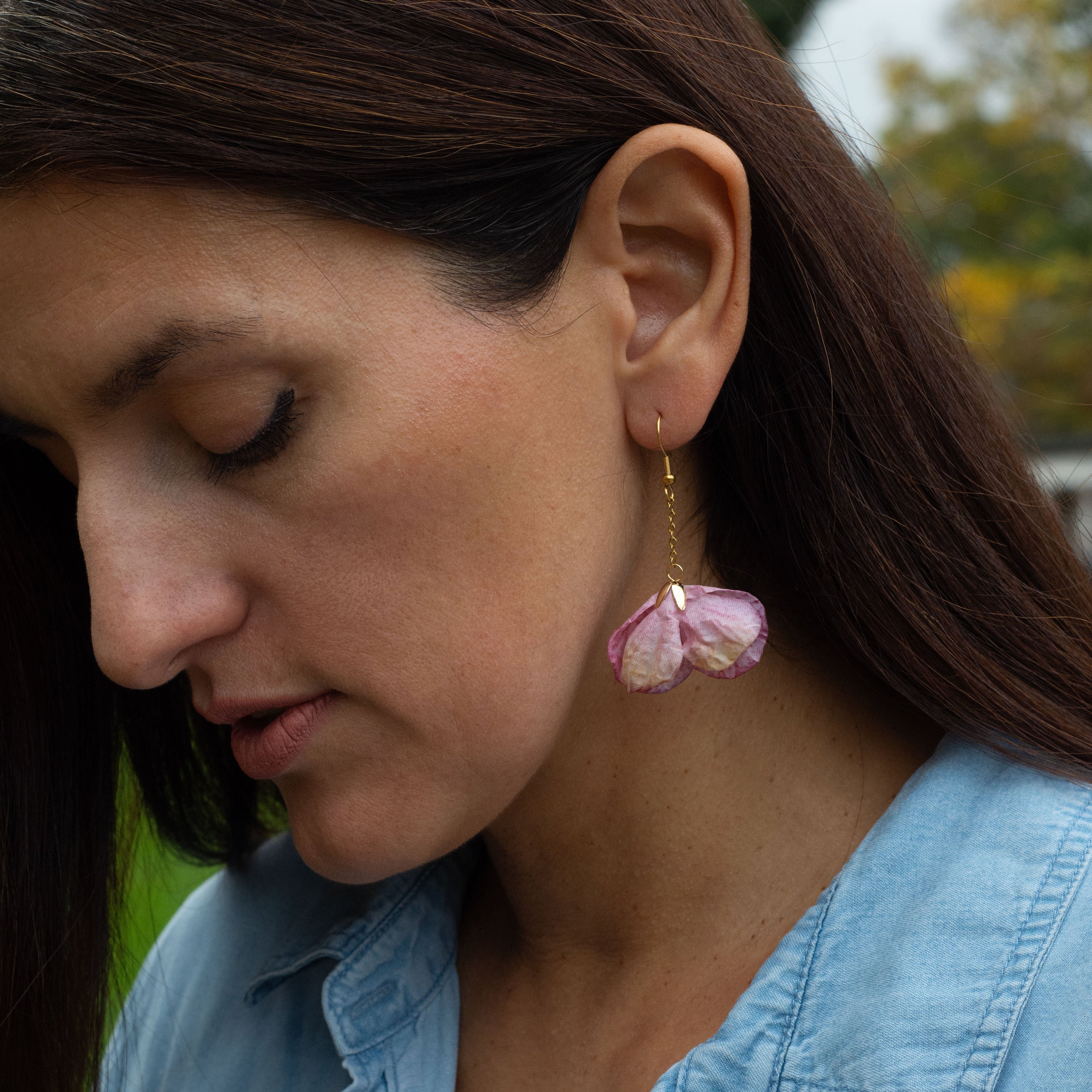 Woman wearing a light blue shirt with a pair of dangly earrings flower shape