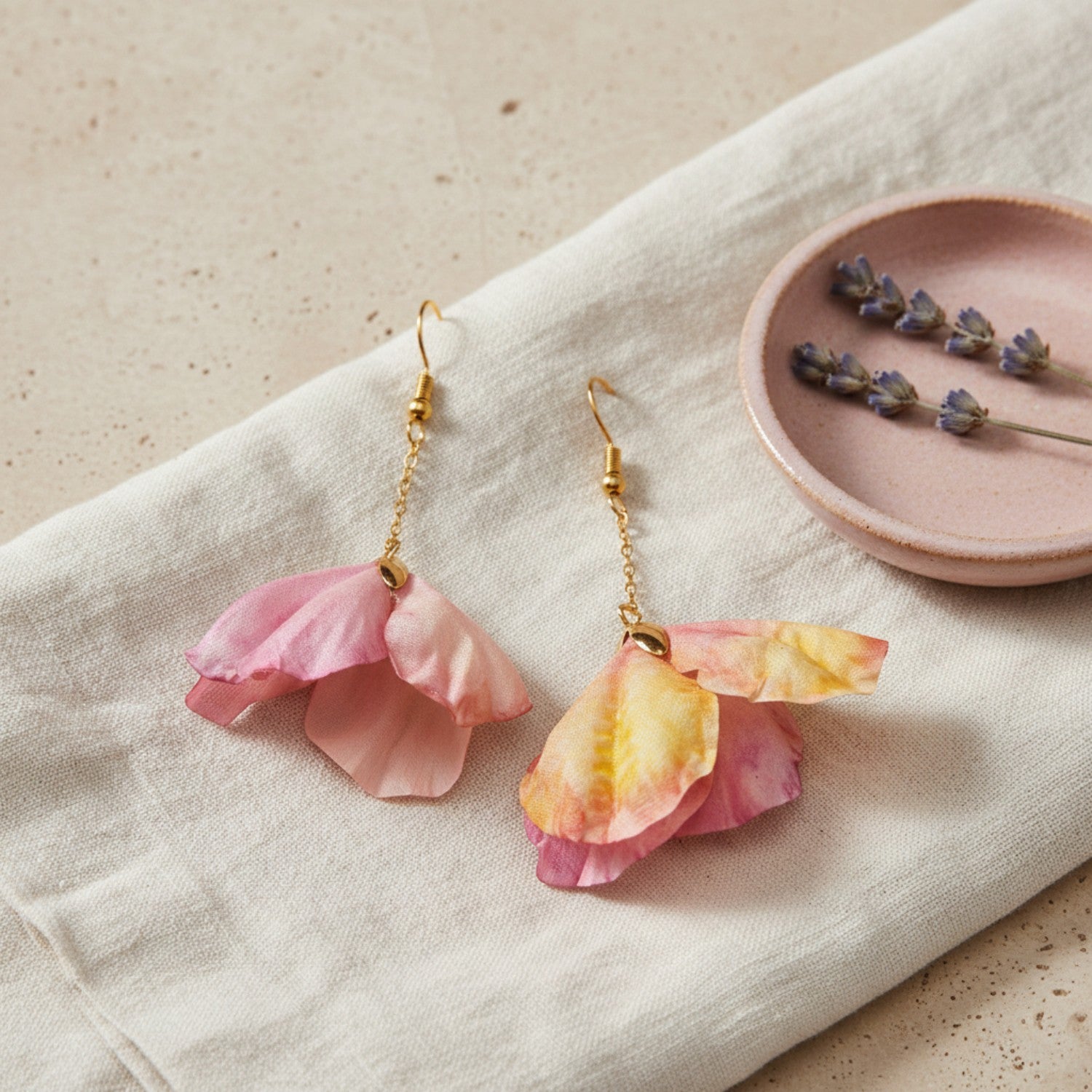 Floral earrings on a light fabric background with a small dish of dried flowers.